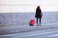 The girl walks on the sidewalk with a red travel bag on wheels. Baggage young tourist in a modern stylish suitcase. Traveler is in