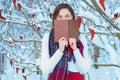 The girl walks through the winter forest. She covered her face with a book. Learning concept. Winter`s tale
