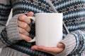 Girl in a warm cardigan is holding white mug in hands.