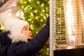 Girl in a warm hat looks at the flame of a gas burner warming at a Christmas market in the city, warms your hands. lights of Royalty Free Stock Photo