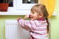 Girl warm one's hands near radiator.