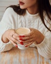 Girl in warm sweater is holding hot cup of coffee or cocoa in hands.