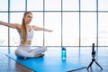 Girl warming up while sitting on yoga mat in front of the camera phone. Female sports blogger records fitness online stream. Home