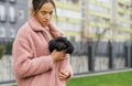 Girl warms up a little curly puppy under his coat on a cool spring day. Lady with a dog under a jacket walks down the street, a