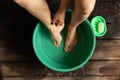 Girl washes her feet in a green bowl on the wooden floor of the house, foot care