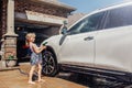 Girl washing car on driveway in front house on sunny summer day Royalty Free Stock Photo