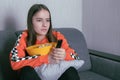 Girl watching tv, sitting with the remote control on the couch, holding popcorn