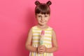 Girl with water ice cream looking directly at camera, posing isolated over pink wall, wearing striped white and yellow dress, Royalty Free Stock Photo