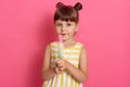 Girl with water ice cream looking directly at camera, posing isolated over rosy background, dresses striped white and yellow Royalty Free Stock Photo