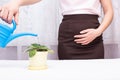 A girl is watering a flower in the office from a watering can and holding on to the bladder, the concept of urinary incontinence