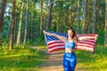 Girl waving American flag.Attractive patriotic American girl wrapped usa flag at summer forest