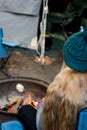 Girl wearing beanie hat roasting large marshmallow on a stick over the campfire firepit. Camping family fun lifestyle Royalty Free Stock Photo