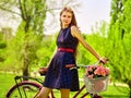 Girl wearing blue polka dots sundress rides bicycle with flowers basket.