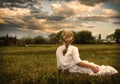 Girl wearing a dress sitting in a pasture