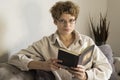 Girl wearing glasses is sitting on the couch and reading a book Royalty Free Stock Photo