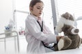 Girl wearing labcoat imitating doctor while examining teddybear with stethoscope at hospital