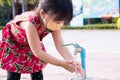 Girl wearing orange cloth face mask was washing her hands thoroughly with a tap, after cute child finished playing on playground.