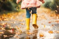 Girl wearing rain rubber boots walking running and jumping into puddle with water splash and drops.