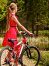 Girl wearing red dress rides bicycle in park. Royalty Free Stock Photo