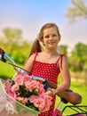 Girl wearing red polka dots dress rides bicycle into park. Royalty Free Stock Photo