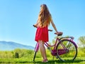 Girl wearing red polka dots dress rides bicycle into park. Royalty Free Stock Photo