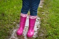 Child in bright pink rubber boots and blue jeans frolic in a dirty puddle