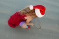 Girl wearing a Santa hat drawing a heart in the sand at the beach Royalty Free Stock Photo