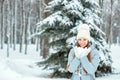 A Girl Wearing Warm Winter Clothes And Hat Blowing Snow In Winter Forest, horizontal. Model with a beautiful smile near the Christ Royalty Free Stock Photo