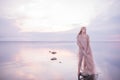 A girl in a weightless light fabric of pastel tones in the water of a calm pond with a reflection of the sunset gentle sky in the Royalty Free Stock Photo