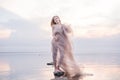 A girl in a weightless light fabric of pastel tones in the water of a calm pond with a reflection of the sunset gentle sky in the Royalty Free Stock Photo