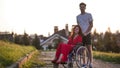 Girl In A Wheelchair Cute Talking To Her Young Man On The Background Of The House, Green Grass