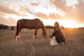 A girl in a white airy dress stands next to a horse and poses in the forest at sunset, like in a fairy tale. Well Royalty Free Stock Photo