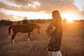 A girl in a white airy dress stands next to a horse and poses in the forest at sunset, like in a fairy tale. Well Royalty Free Stock Photo