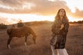 A girl in a white airy dress stands next to a horse and poses in the forest at sunset, like in a fairy tale. Well Royalty Free Stock Photo