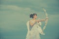 Girl in white angels dress, cupid with wings aiming with bow and arrow on a sky background. Valentines day concept Royalty Free Stock Photo