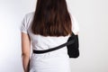 A girl on a white background with a black supporting medical bandage after a dislocation of the shoulder joint and a