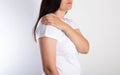 A girl on a white background is holding her shoulder and has aching pain. The concept of bursitis and pain of the