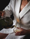 Girl in a white bath robe puring herbal tea in a transparent glass Royalty Free Stock Photo