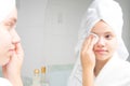 Girl in a white bathrobe and a towel on her head, near the mirror in the bathroom, cleans her face with a cotton swab Royalty Free Stock Photo