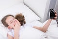 Girl in a white bed, yawning, holding an alarm clock Royalty Free Stock Photo