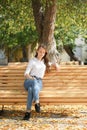 a girl in a white blouse and blue jeans sits on a wooden bench in autumn Park square Royalty Free Stock Photo