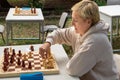 A girl in a white blouse is sitting at a table playing chess in nature Royalty Free Stock Photo