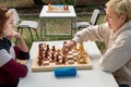 A girl in a white blouse is sitting at a table playing chess with a teenage girl in nature mom and daughter are intellectuals Royalty Free Stock Photo