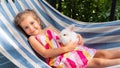 A girl with a white bunny lies on a hammock in the summer on a sunny day. White fluffy decorative rabbit in the arms of a little Royalty Free Stock Photo