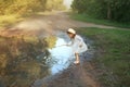 Girl in white checkered dress and hat is playing with a stick in a muddy puddle after the rain. Royalty Free Stock Photo
