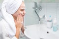 Girl in a white coat, cleans her face with foam, in the bathroom, near the tap and sink Royalty Free Stock Photo