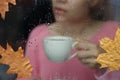 Girl with white cup behind wet window with raindrops on glass