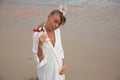 Girl in white dress on the beach sitting on the sand holding a red flower Royalty Free Stock Photo