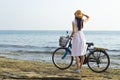 Girl in a white dress with a bicycle on the seashore.