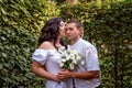 Girl in white dress gently hugs her boyfriend& x27;s neck and kisses him on the cheek. Newlyweds in the park. Portrait